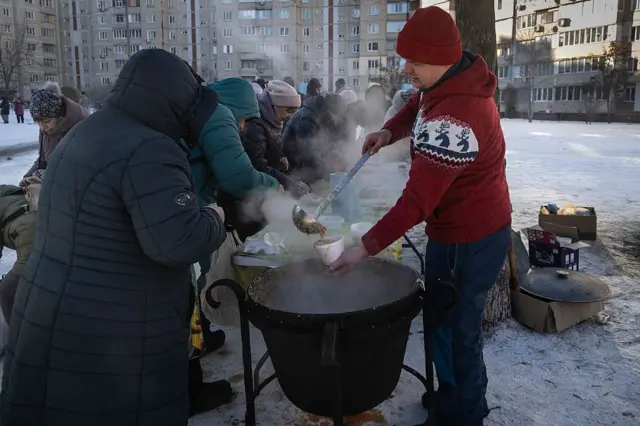 Люди стоять у черзі на вулиці біля казанка з гарячою їжею