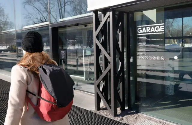 Девушка с рюкзаком за спиной проходит мимо здания со стеклянными стенами