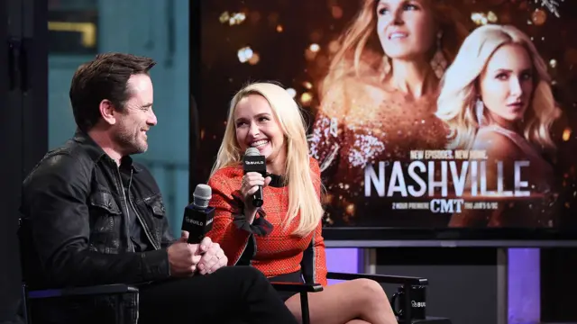 Charles Esten y Hayden Panettiere en un evento de prensa con un cartel de "Nashville" detrás.