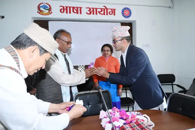 भाषा आयोगका अध्यक्ष गोपाल ठाकुरलाई फूल दिँदै एक व्यक्ति