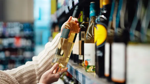 वाइन की बोतल पर कीमत देखती एक महिला