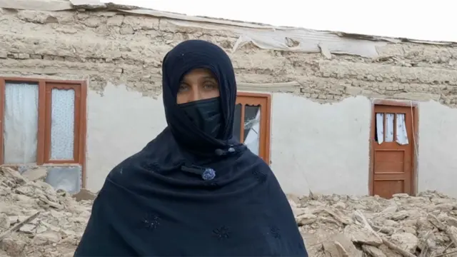 تصویر زنی زلزلهزده در مقابل خانه ویرانهاش. او چادر سیاه به سر دارد وصورتش را با چادرش پوشاندهاست.