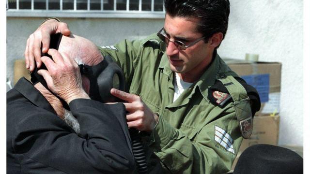 جندي إسرائيلي يساعد مسنا على ارتداء قناع واق من الغاز تحسبا لتعرض البلاد لهجمات بأسلحة كيميائية من قبل العراق في عام 1991