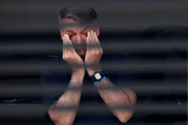 Bolsonaro leva as mãos ao rosto, atrás da grade de sua casa