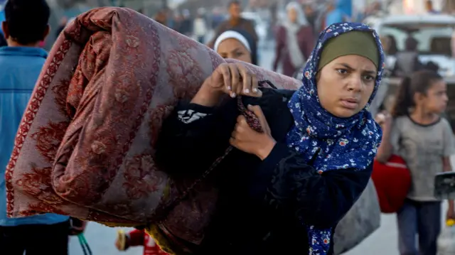 Жительница Газы в синем платке с большим свитком из одеял за спиной