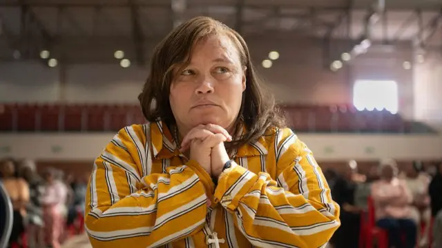 
Kelly Smith siddon for courtroom wit her hands togeda, she wear one striped shirt.