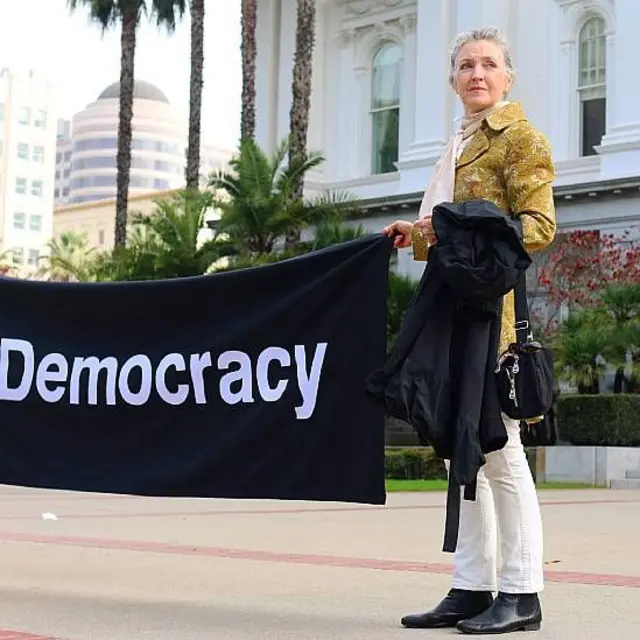 Rebecca Solnit durante una protesta con un cartel que dice "democracia"