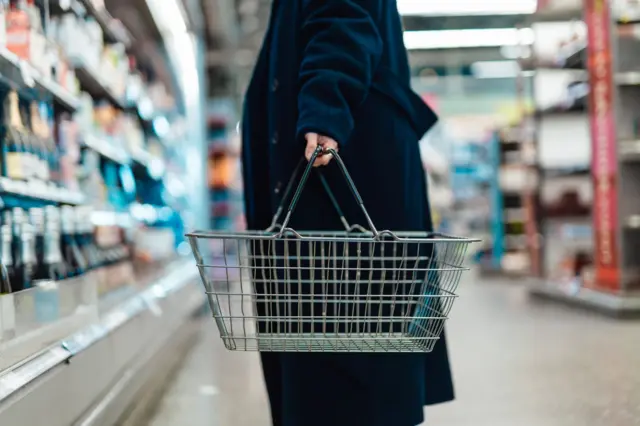 Persona con un canasto de compras en el supermercado.