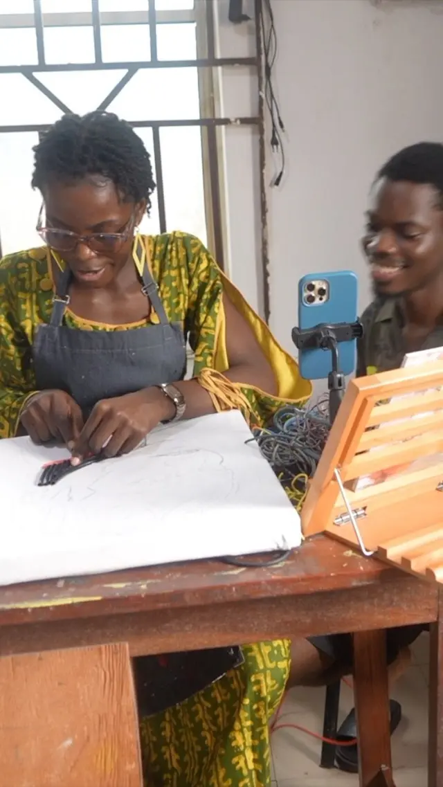 Patience Adekunle wọ asọ ankara alawọ yẹlo, o n ge waya lati fi ya aworan, ọkunrin kan duro ti lẹgbẹ.
