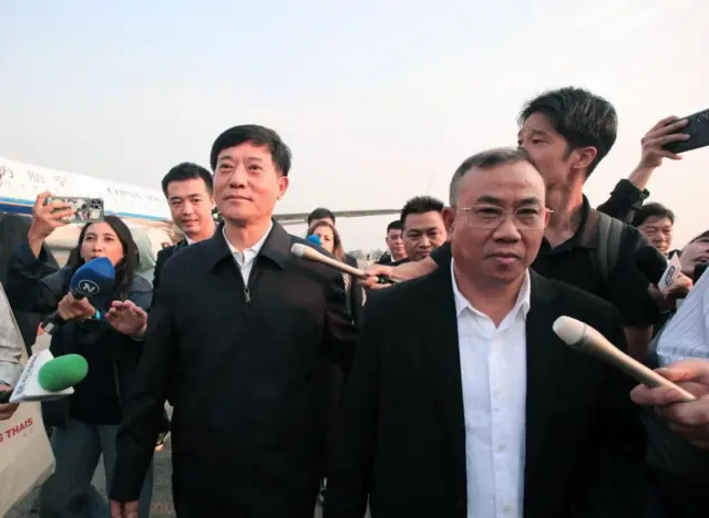  थाई-म्यान्मार सीमा क्षेत्रबाट उद्धार गरिएका चिनियाँहरूलाई लिन पुगेका चिनियाँ अधिकारीहरू, पृष्ठभूमिमा चिनियाँ विमान देखिन्छ