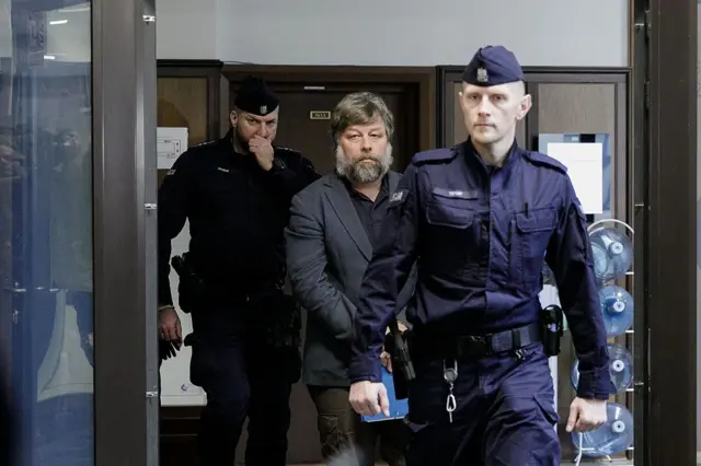 Працівники служби охорони виводять Бутягіна коридором будівлі суду. Один охоронець іде попереду, інший супроводжує затриманого позаду.