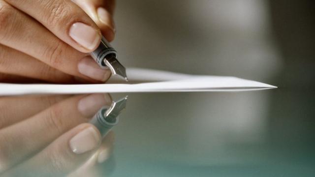 Mão de mulher segurando caneta e escrevendo em folha de papel