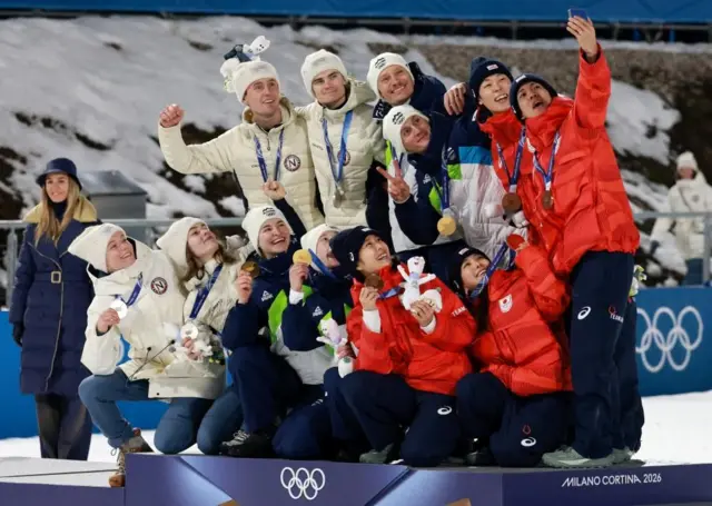 メダルを首から下げた各国選手4人ずつ計12人が、表彰台の一番高いところに前後2列で並び、右端にいる二階堂が持つカメラに向けて笑顔を見せている