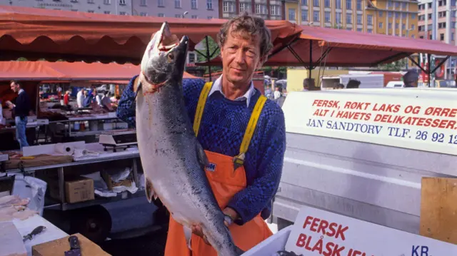 A fishmonger holding a big salmon in Bergen Market, Norway.