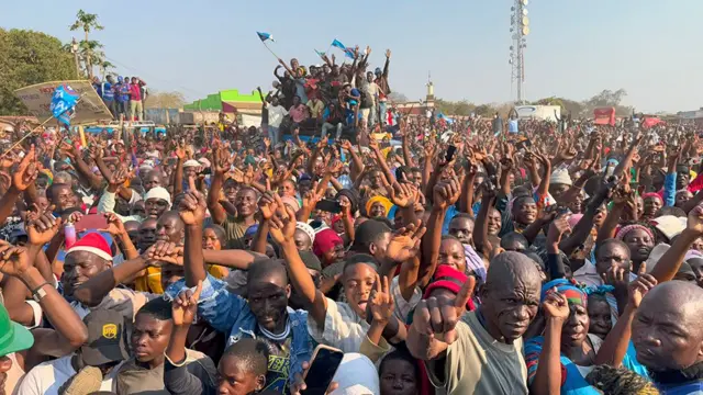 Une foule nombreuse lors d'un rassemblement électoral agite les mains en l'air. Certains, à l'arrière-plan, se détachent des autres, à l'arrière d'un camion.