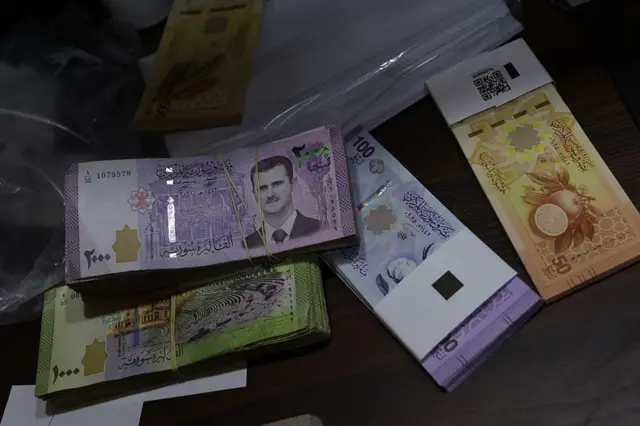Eski ve yeni banknotların bir arada olduğu bir fotoğraf. Bir banknotun üzerinde Beşar Esad'ın takım elbiseli fotoğrafı var. Yeni banknotlardaysa portakal ve pamuk görünüyor.
