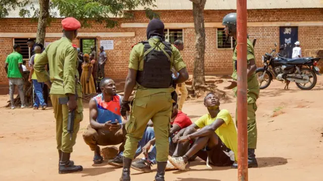Tanzanian police officers (in green uniform and holding guns) surround a group of young voters (all seated) following their arrest in Kigoma in 2024