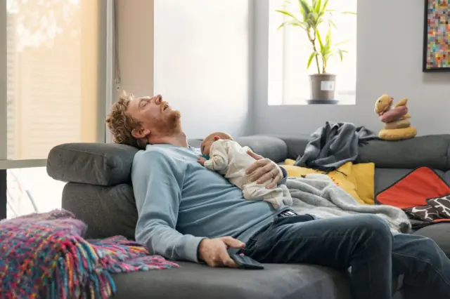 втомлений батько заснув на дивані з немовлям на руках