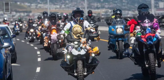 People drive motorbikes in a convoy. Plush toys are fastened on to the bikes.