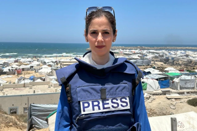 Ghada Al-Kurd çadır kentin önünde üzerinde gazeteci yeleğiyle poz veriyor