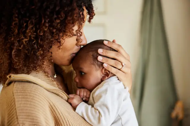 Mulher com bebê no colo, dando beijo na testa dele