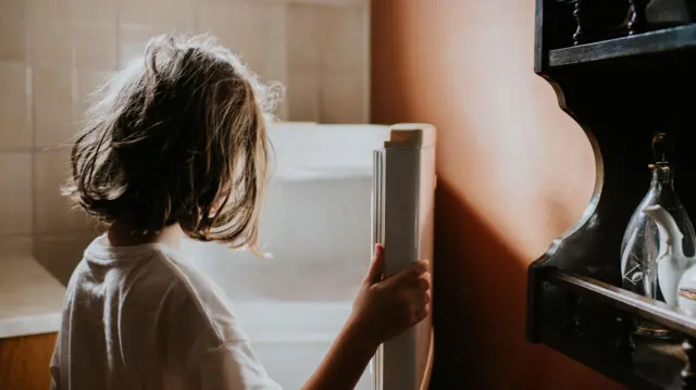 Uma menina de costas abre uma geladeira vazia.