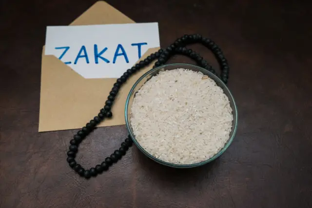 Concept musulman Zakat écrit sur du papier blanc sur une enveloppe brune, un bol de riz et des chapelets pour payer la zakat.