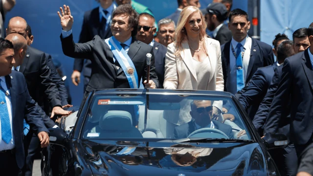 Milei desfilando em um carro aberto ao lado da irmã. Ao redor deles há vários seguranças