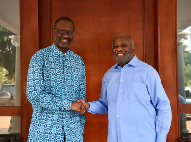 Tidjane Thiam en chemise Wax (gauche) et Laurent Gbagbo, barbe poivre sel,chemise bleue claire, qui se serrent la main, sourire au visage.