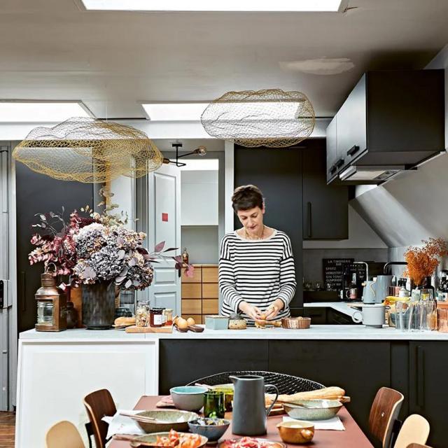 Fotografia colorida mostra uma bancadapixbet slotuma cozinha aberta para a sala e uma mulher branca cozinhando