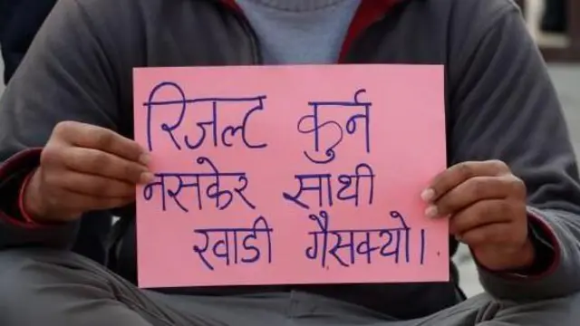 'रिजल्ट कुर्न नसकेर साथी खाडी गैसक्यो' लेखिएको कागज हातमा लिएर विरोधप्रदर्शनमा बसेका एक व्यक्ति