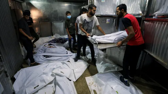 يقف الناس في المشرحة بالقرب من جثث الضحايا في يوم جنازة الفلسطينيين الذين قُتلوا بنيران إسرائيلية أثناء محاولتهم تلقي المساعدة يوم الجمعة