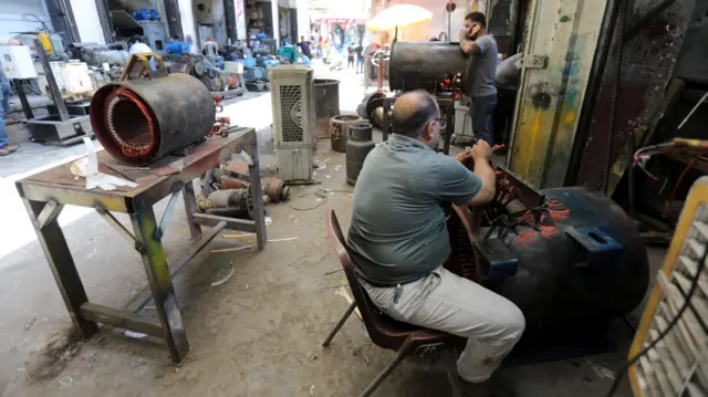 مردی در یک روز گرم در مرکز بغداد، عراق، یک ژنراتور برق را در یک کارگاه تعمیر می کند.