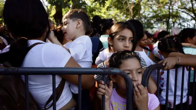 Two girls hold one barricade as one woman nearby carry one child for di middle of di crowd.