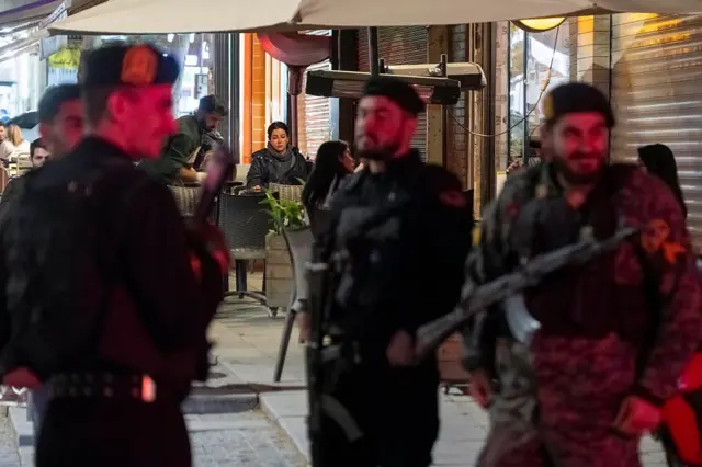 افسران مسلح پلیس ایران در ۱۲ آوریل ۲۰۲۶، در جریان آتشبس میان ایران و ائتلاف ایالات متحده–اسرائیل، در پیادهرویی نزدیک یک کافهٔ روباز در شمال تهران نگهبانی میدهند.