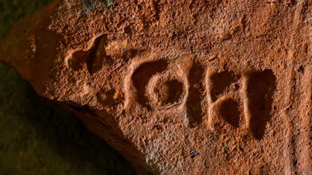 Uma telha vermelha com um 'carimbo' composto por três letras em sua superfície mostrando que era um prédio público e pertencia ao procurador de Londres. Também tem uma série de ranhuras curvas feitas pelo fabricante da telha, arrastando seus dedos sobre ela quando estava sendo produzida
