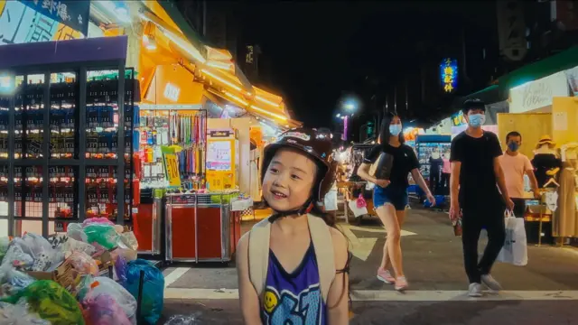 一個帶著頭盔的女孩歪著頭站在夜市裡