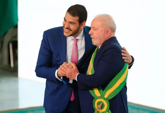 Jorge Messias ao lado de Lula que usa faixa presidencial