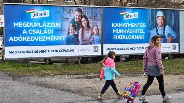 Egy anyuka és a kislánya sétál két óriásplakát előtt. Az egyiken a 'Megduplázzuk a családi adókedvezményt', a másikon a 'Kamatmentes munkáshitel fiataloknak' szlogen áll.