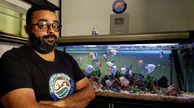 Aquarista Antonio Candido com um aquário atrás e peixes coloridos
