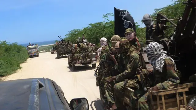 Groupe de membres d'al-shabab habillés en tenue de camouflage, assis à l'arrière de plusieurs camionnettes, armés de fusils et le visage couvert.