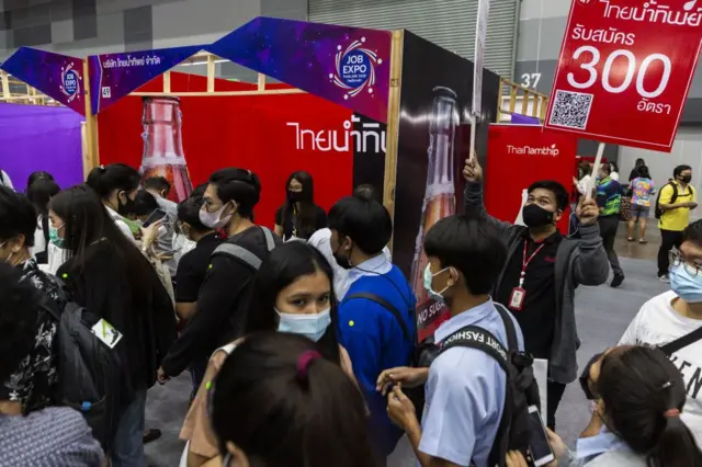 Visitors wearing protective masks walk past a Coco-Cola Co. booth at a recruitment fair organised by Thailand's Ministry of Labor in Bangkok, Thailand, on Saturday, Sept. 26, 2020. 