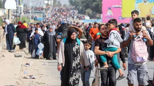 በጋዛ መንገድ ላይ የሚሄዱ ብዙ ሰዎች። ከፊት ለፊት ሁለት ሰዎች ትናንሽ ልጆችን ይዘዋል