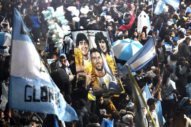 Hinchas argentinos sostienen una pancarta con las imágenes de los futbolistas campeones del mundo Diego Maradona, Mario Kempes y Lionel Messi cerca de la concentración de la Asociación del Fútbol Argentino (AFA) en Ezeiza, Buenos Aires, el 20 de julio de 2026.