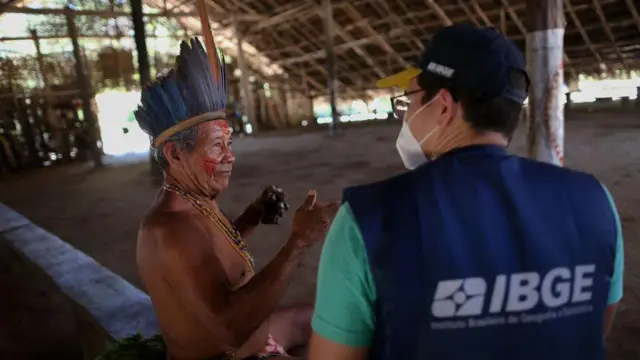 Pesquisador do IBGE conversa com homem indígena  numa aldeia