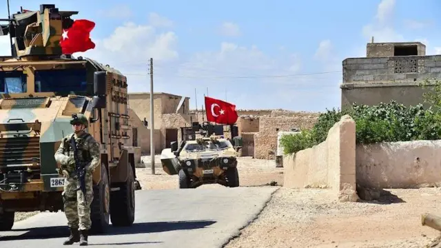 Türk Silahlı Kuvvetleri'ne ait zırhlı araçlar, 18 Haziran 2018 tarihinde Suriye'nin kuzeyinde devriye geziyor. Fotoğrafta iki zırhlı araç ve elinde tüfek tutan bir asker var.