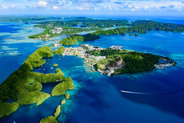 Foto colorida mostra ilhas verdes com área construída, vistas de cima, em um mar muito azul