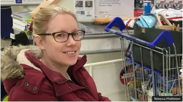 Rebecca agaragara yifubitse ikote ritukura ry'imbeho ndetse na lunettes ari nko mu iduka.