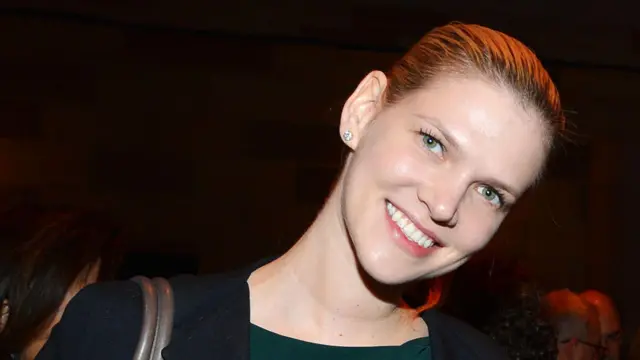 Nadia Marcinko stoi zwrócona twarzą do kamery, z lekko przechyloną głową, ubrana w ciemną marynarkę nałożoną na zieloną bluzkę i małe kolczyki.