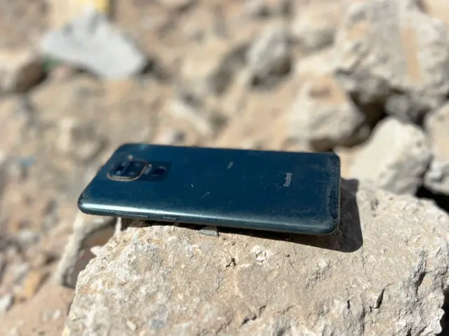 がれきの上に砂で薄汚れたスマートフォンが画面を伏せて置いてある